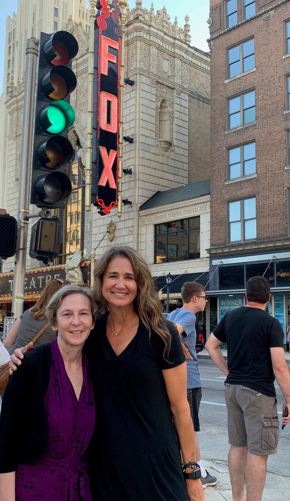 Two female coworker friends stand in front of Fox Theater smiling and in a friendly embrace