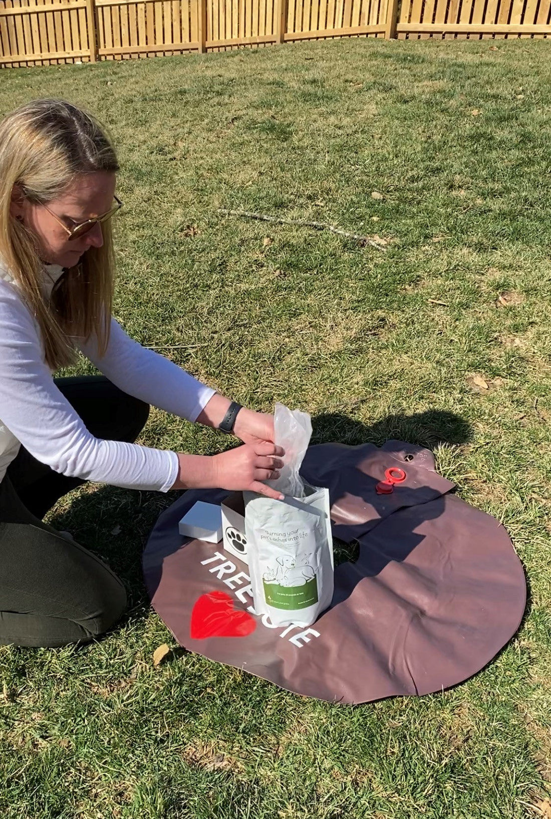 Woman kneeling in the grass opening a bag of Treebute organic soil blend with her memorial tree
