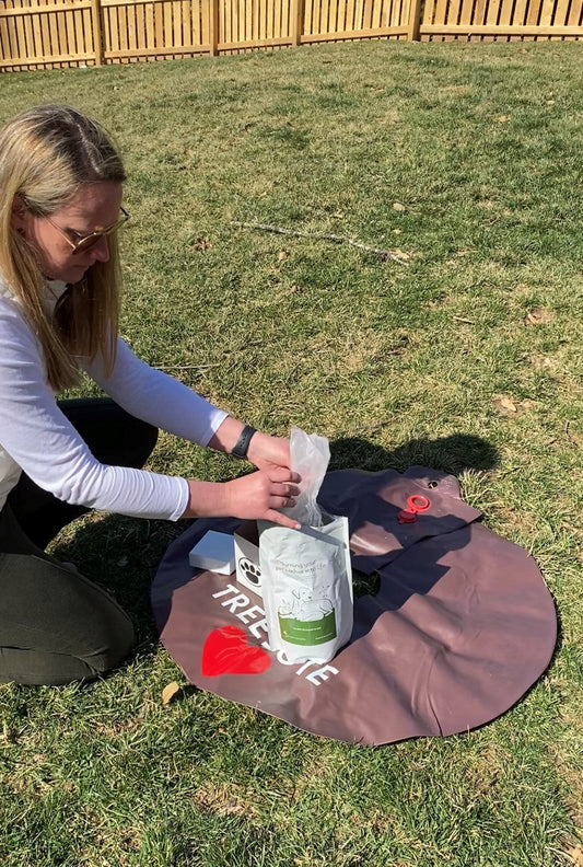 Woman kneeling in the grass opening a bag of Treebute organic soil blend with her memorial tree