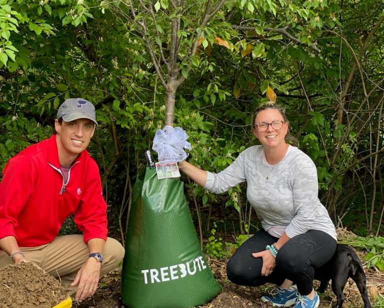 Treebute gift recipients posing and smiling with their memorial tree gift in a backyard garden setting.
